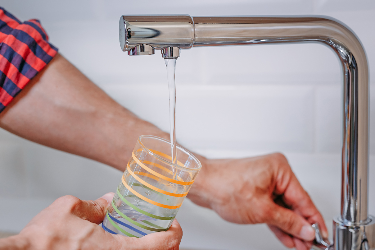 Close up of man pouring glass of water from tap at a kitchen sink.