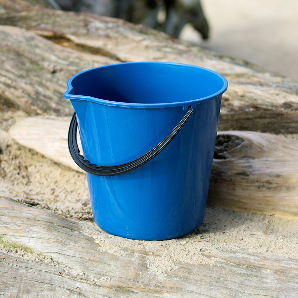 Navy 10 litre bucket with black handle sitting on top of a log.